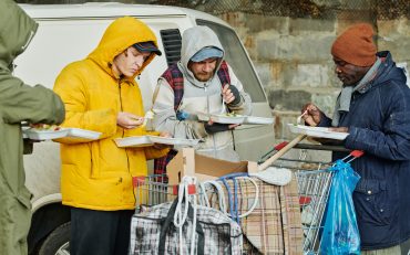 Group of homeless people eating hot food together outdoors, they getting food from charity community
